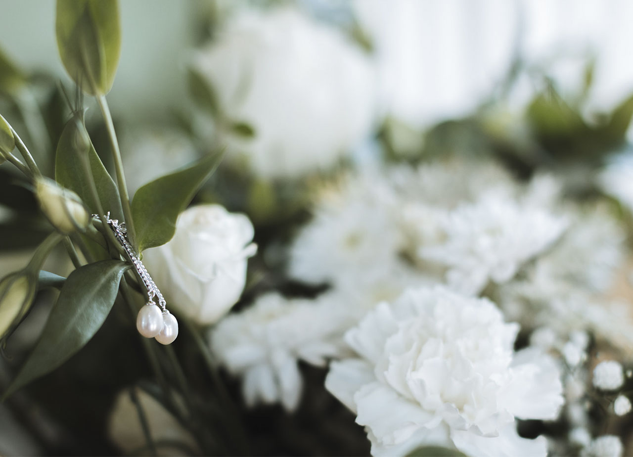 detalle de pendientes de perlas y diamantes una novia sobre flores blancas